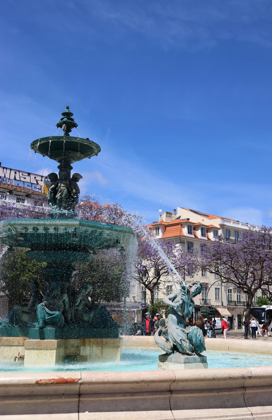 Ornate Lisbon fountain near jacaranda trees and historic architecture